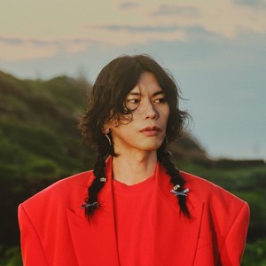 Headshot of Kenshi Yonezu in a bright red suit